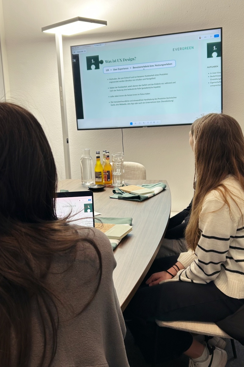 Schülerinnen sitzen im Meetingraum und schauen sich eine Präsentation an.