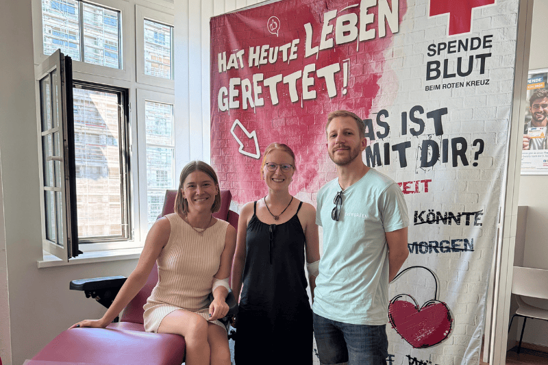 Blutspende_Evergreen-Team_August-2025 3 Personen vom Evergreen-Team vor einem Banner der Blutspende-Einrichtung, auf dem steht: Hat heute Leben gerettet.